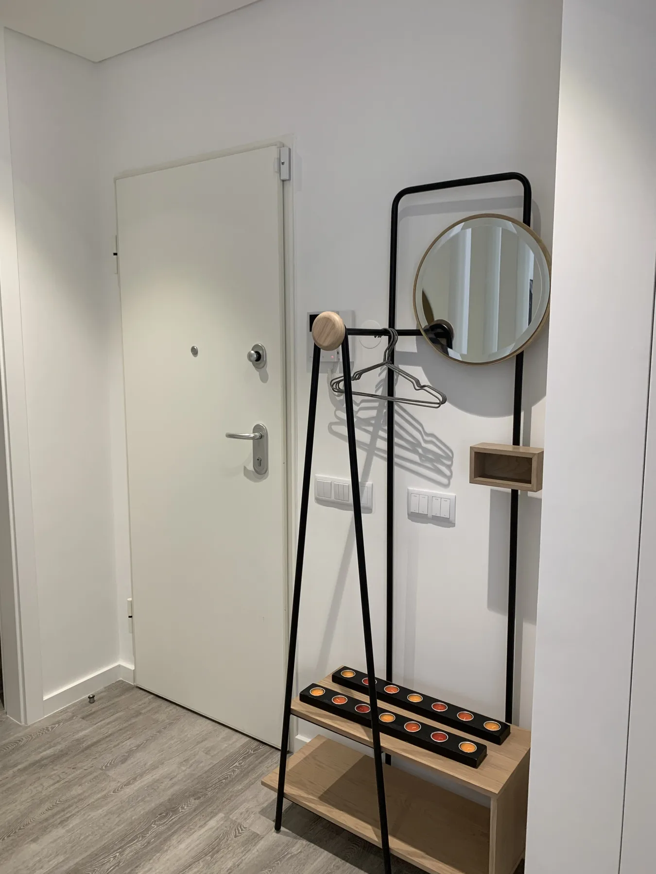 Entrada de un apartamento con una puerta, un espejo redondo y una consola pequeña.