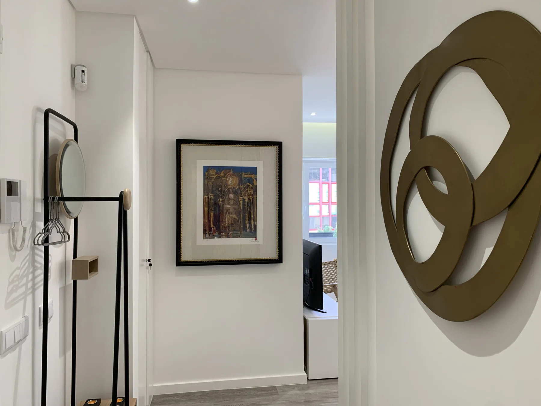 Un pasillo luminoso de apartamento con una obra enmarcada y un espejo de pie.