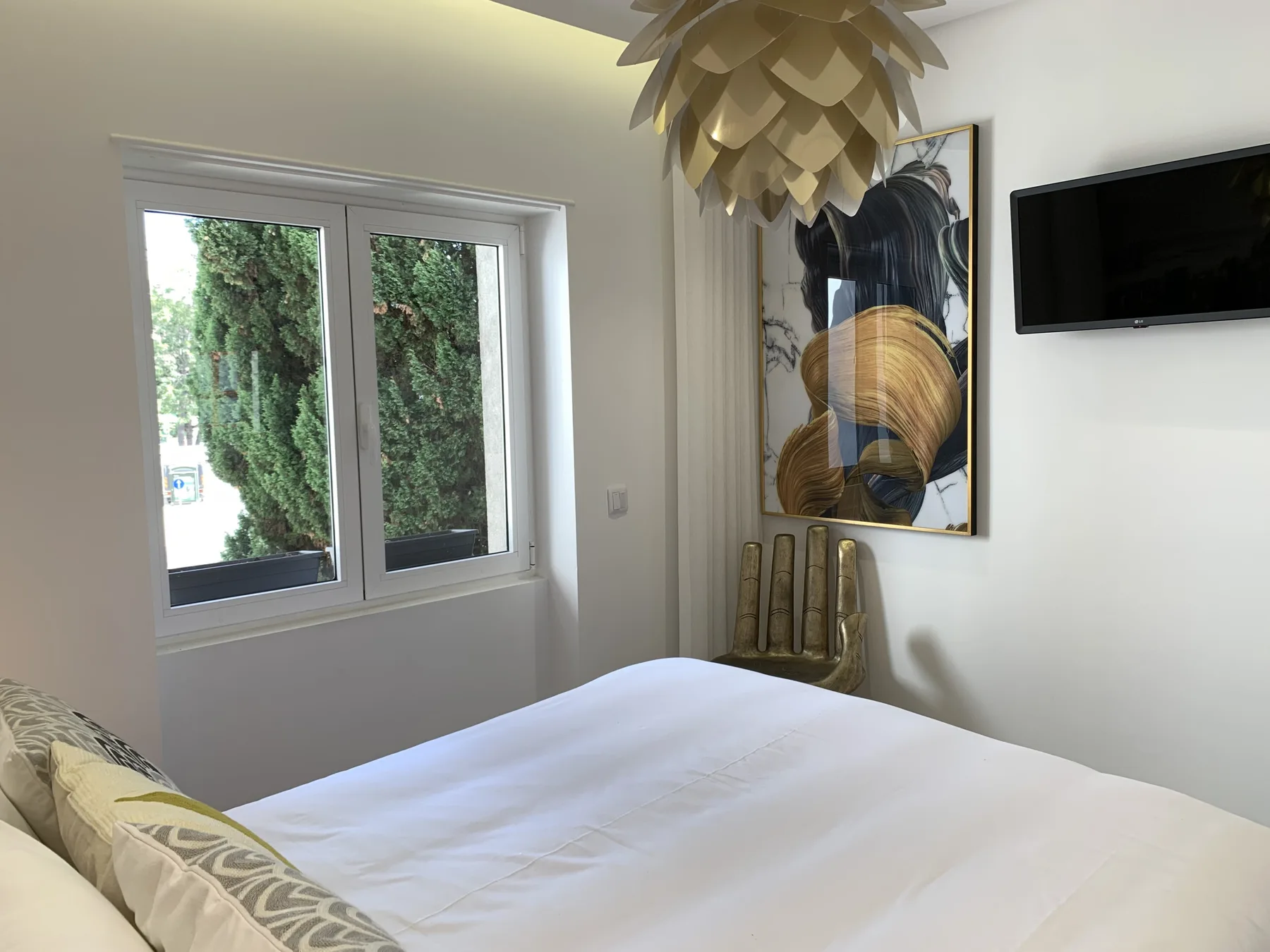Un dormitorio con una cama blanca, una obra enmarcada y un televisor en la pared.