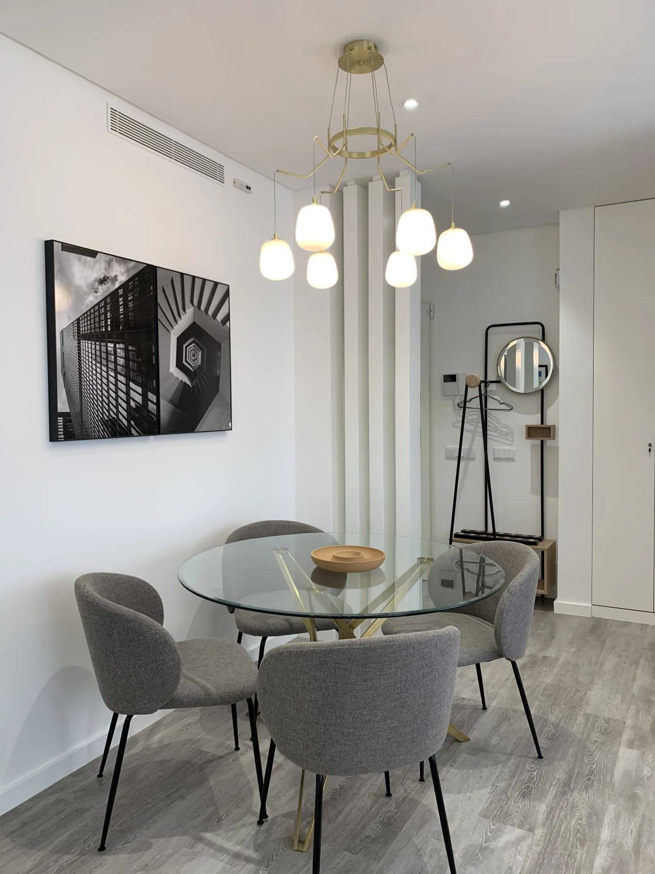 Un comedor con una mesa de cristal y asientos tapizados bajo lámparas colgantes.