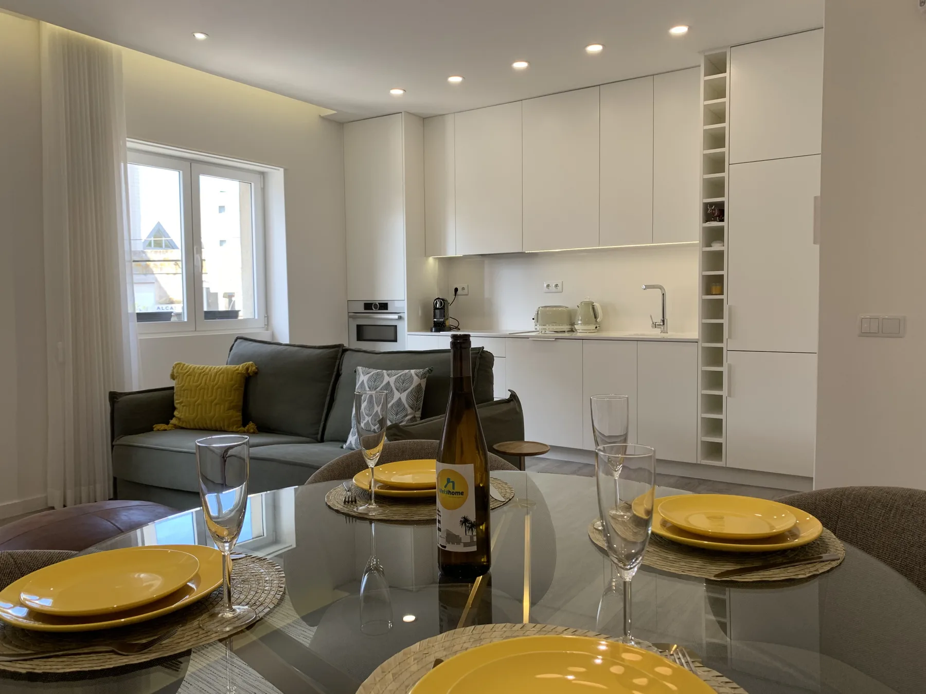 Un comedor con la mesa puesta está frente a una sala de estar y una cocina compacta.