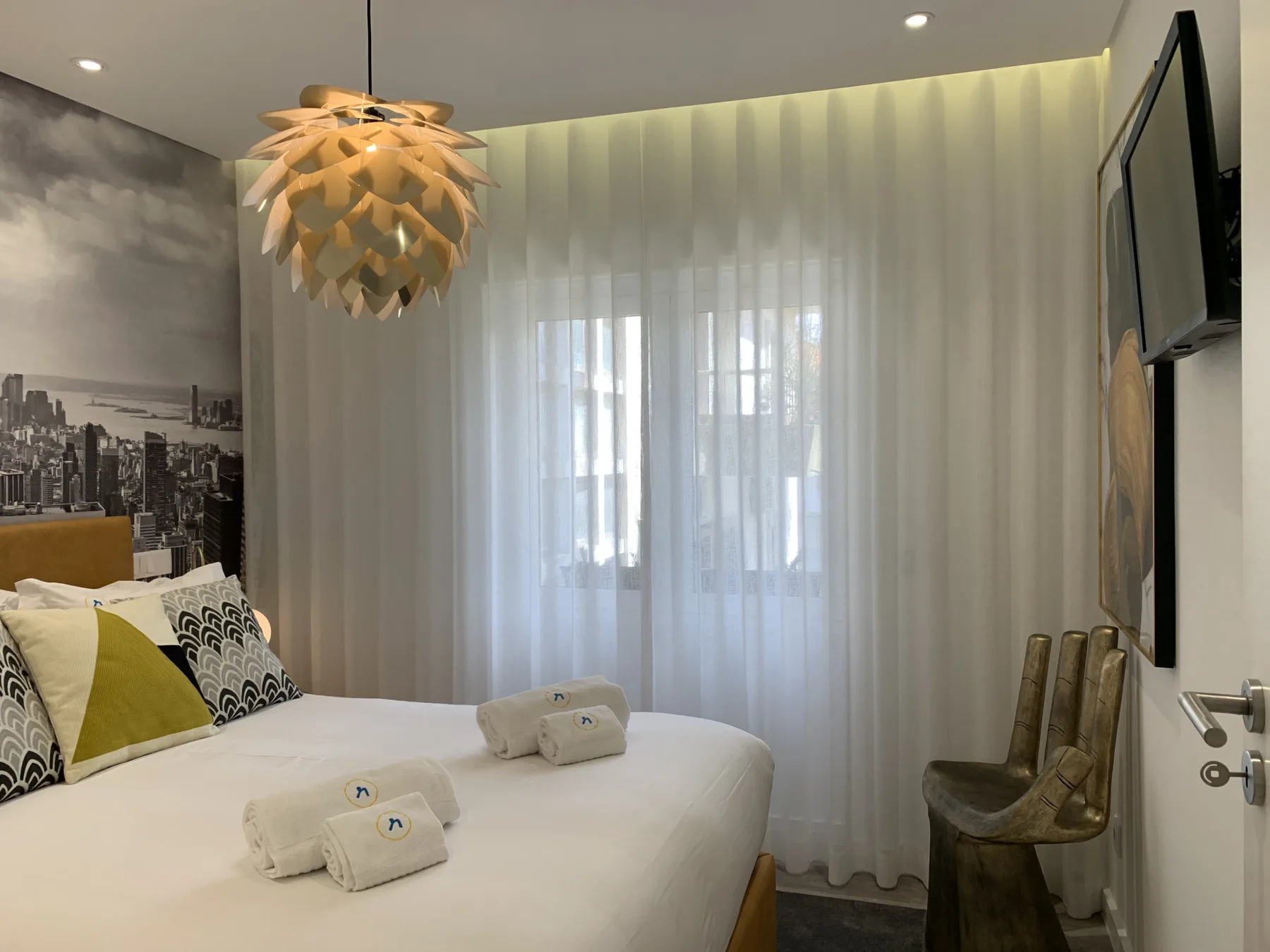 Un dormitorio con una cama grande, cojines estampados y cortinas translúcidas.