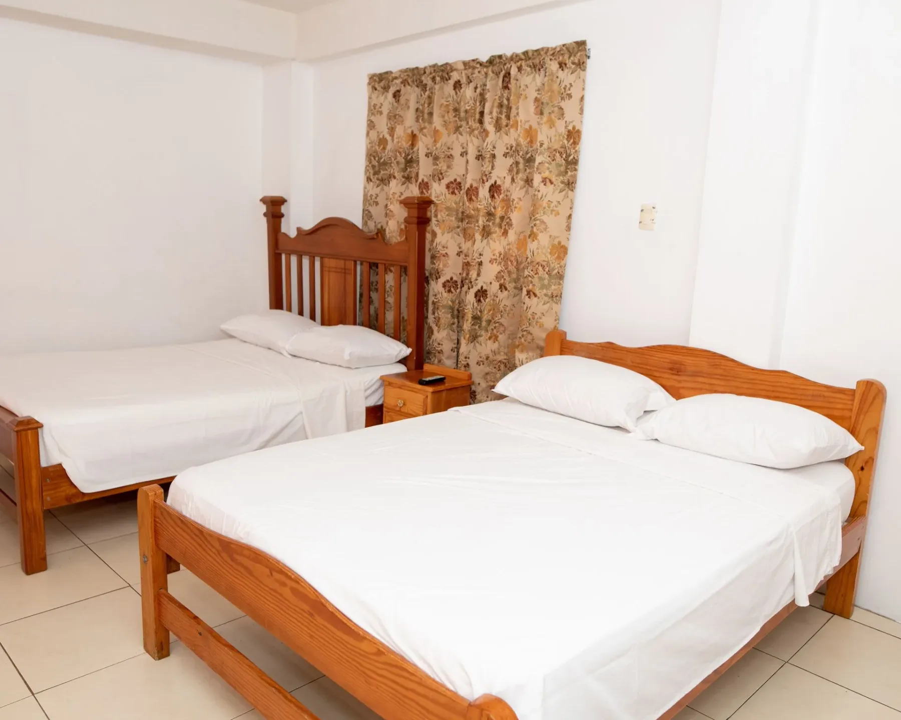 Bedroom with two wooden beds and a patterned curtain.
