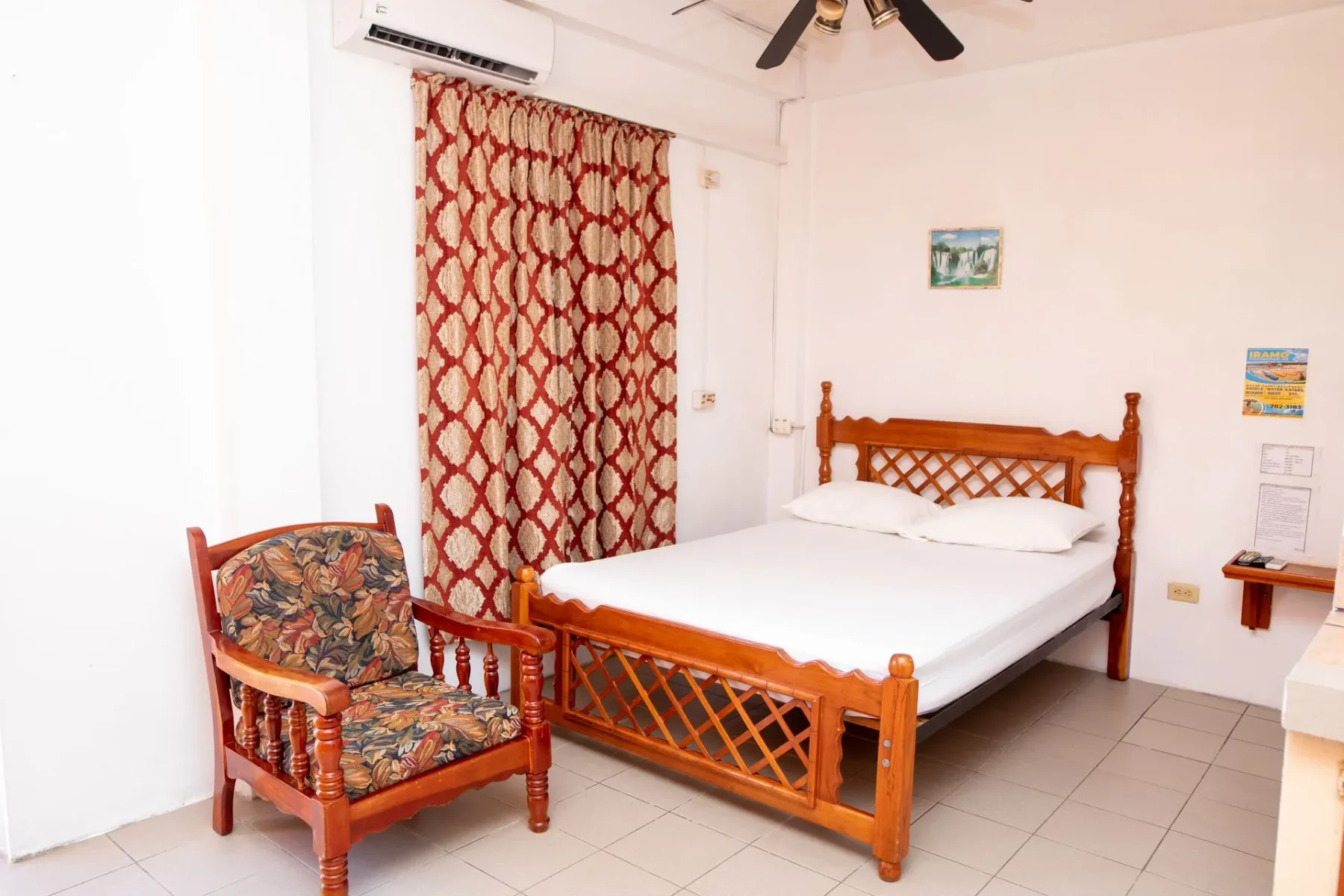 Dormitorio con una cama de madera tallada, cortinas estampadas y un sillón con estampado floral.