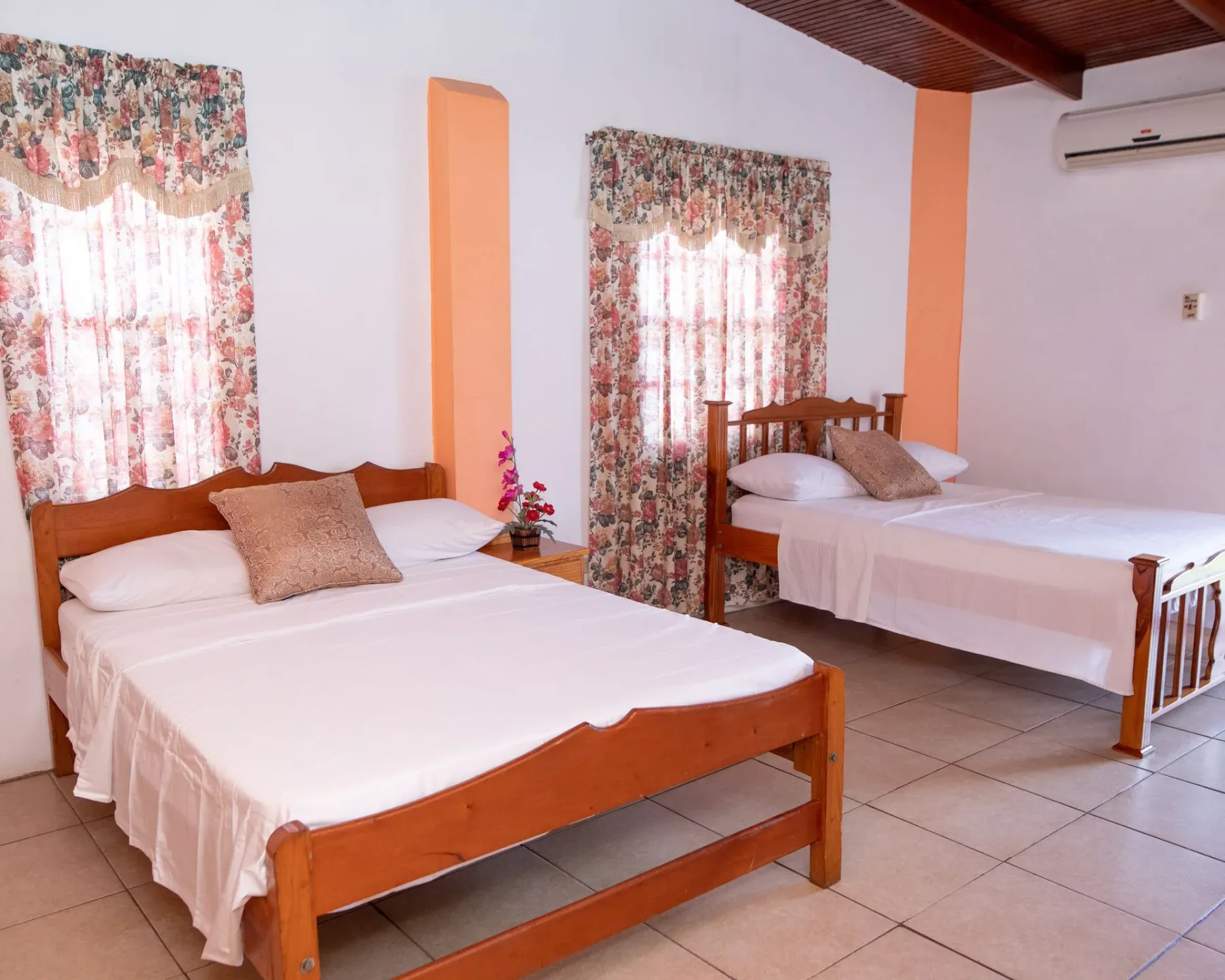 Guest room with two wooden beds, white bedding, and floral curtains.