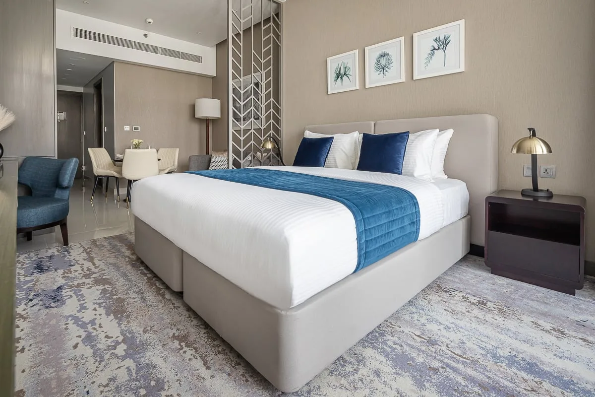 Un dormitorio con una cama bien tendida, una manta azul y láminas botánicas enmarcadas.