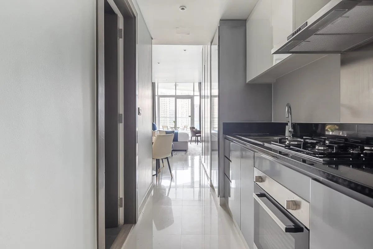 Una cocina estrecha da a un comedor luminoso con una mesa y sillas.