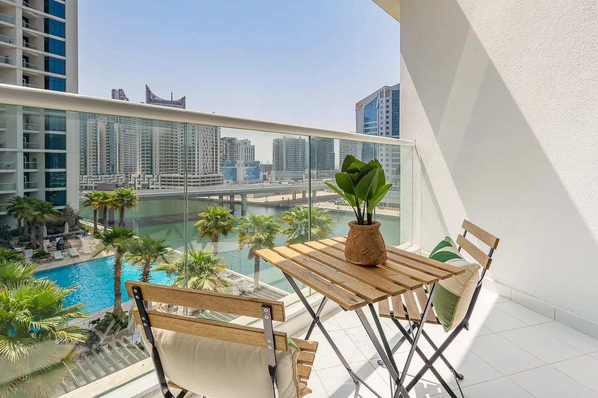Balcón con una mesa y sillas junto a una vista de la piscina y los edificios.