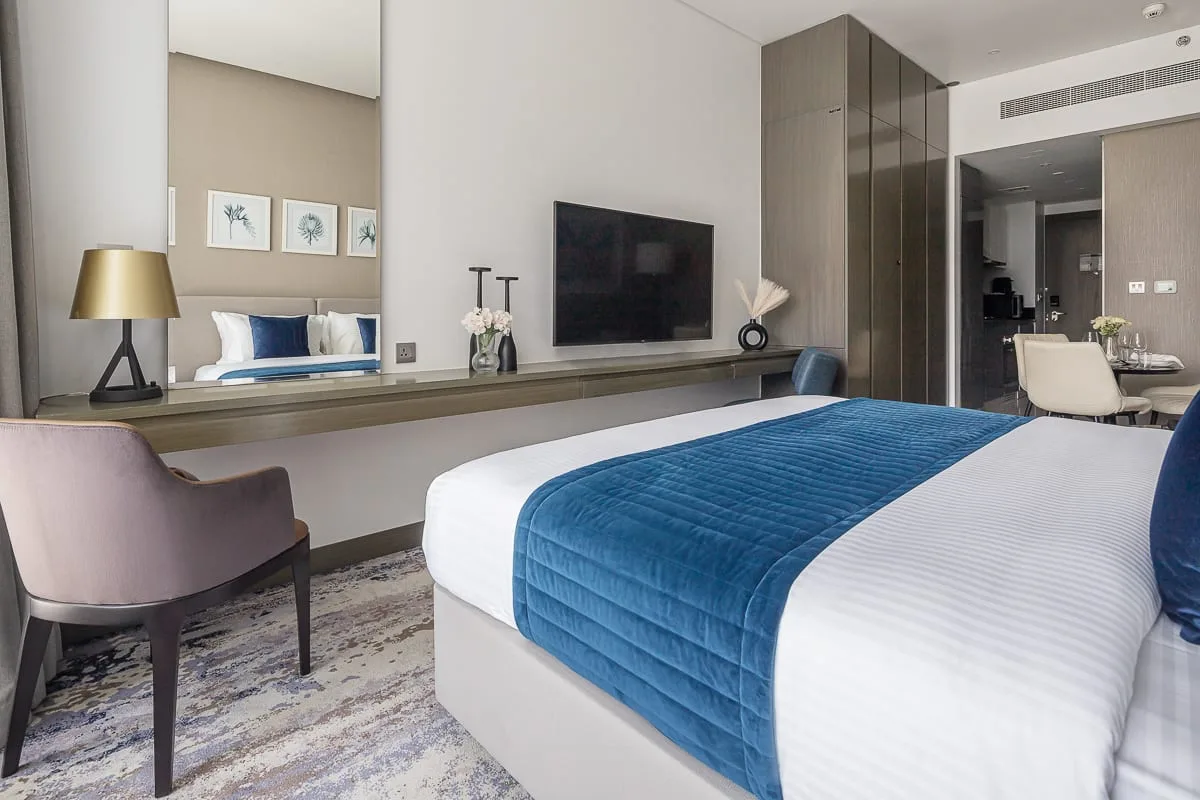 Un dormitorio con una cama, una colcha azul y un televisor en la pared.