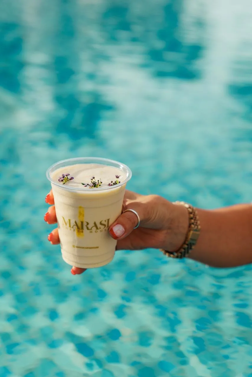 Una mano sostiene una bebida cremosa sobre el agua turquesa de una piscina.