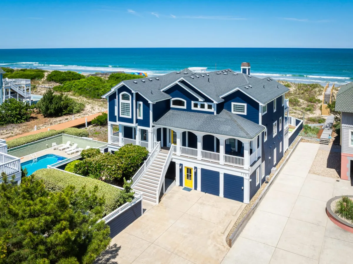 Una gran casa azul junto a la playa mira al océano, con una piscina cercana.