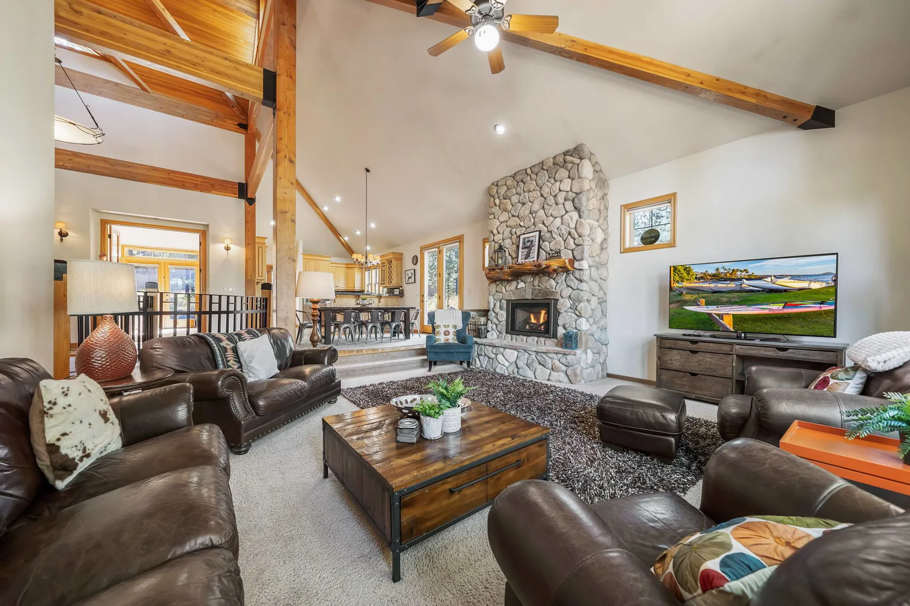 A spacious living room features leather seating, a stone fireplace, and a television.