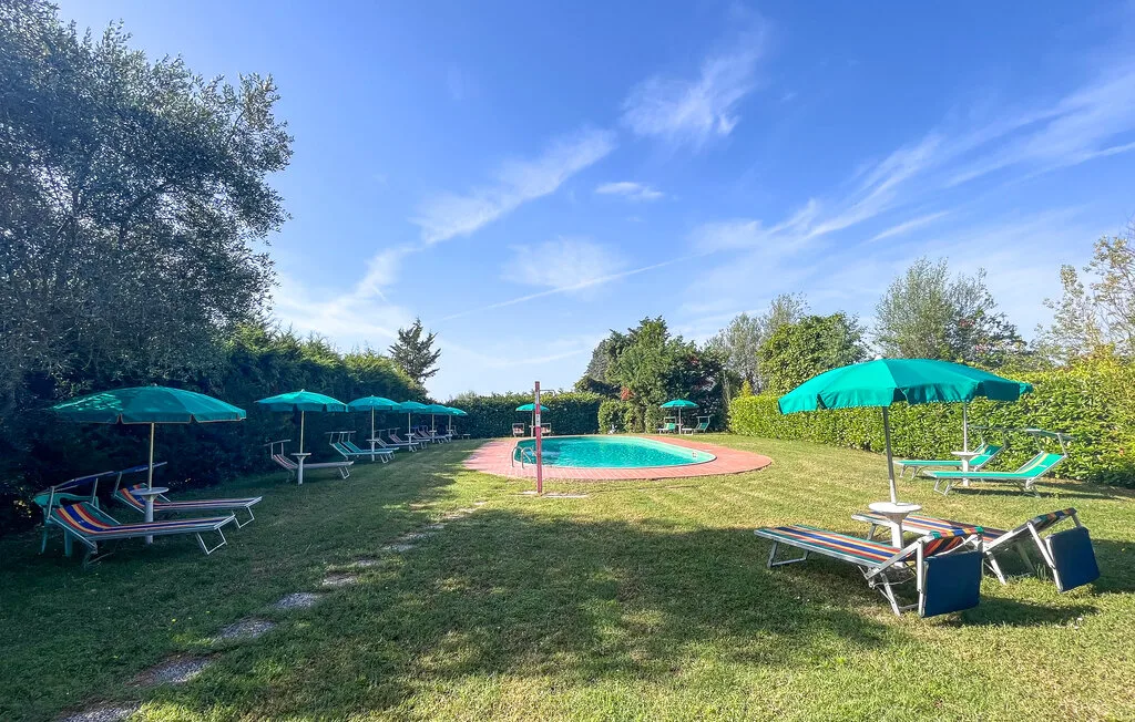 Una piscina al aire libre está en un jardín de césped con asientos a la sombra.