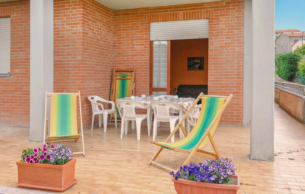 Un patio de ladrillo con sillas plegables de colores, una mesa y flores en macetas.