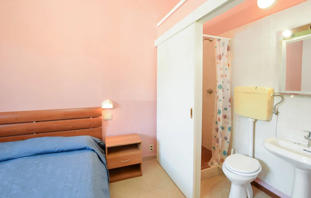 Se ven un dormitorio y un baño, con una cama junto al inodoro y el lavabo.