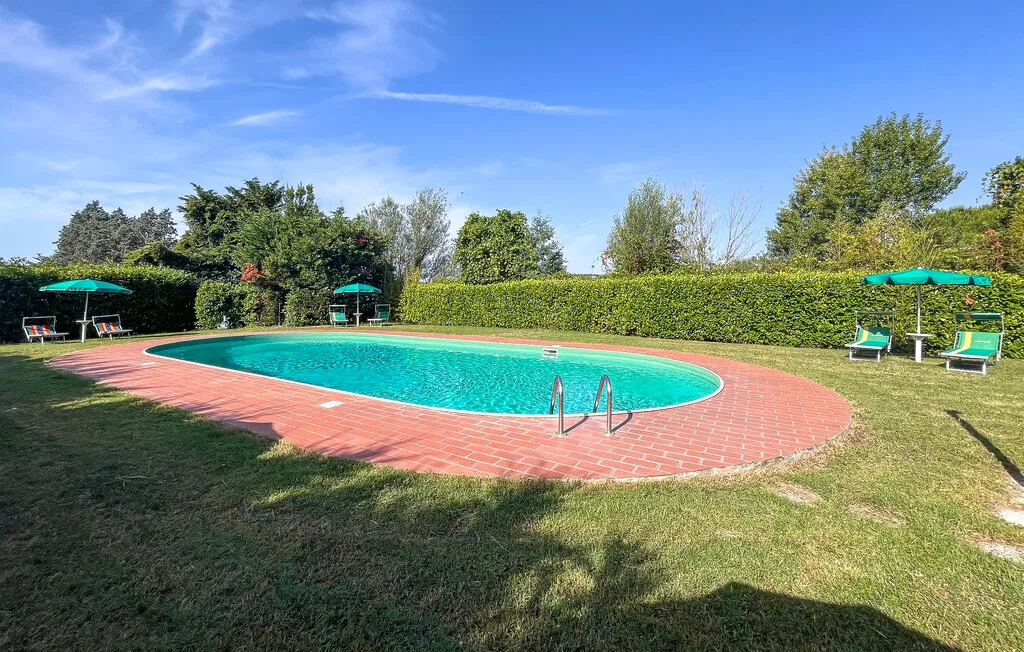 Piscina al aire libre rodeada por una terraza de ladrillo y césped.