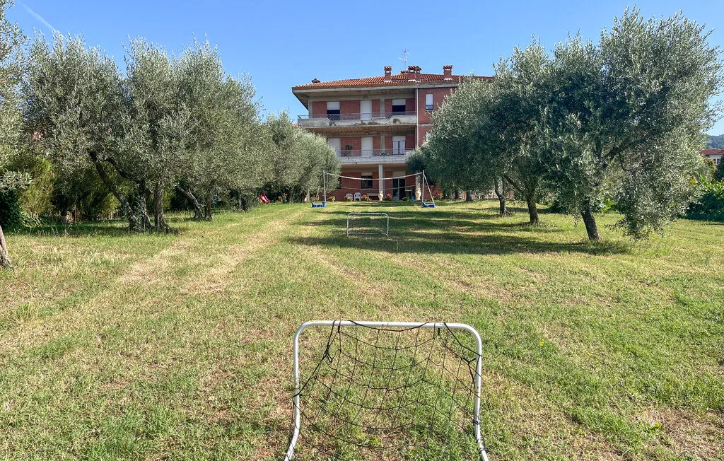 Una zona de juegos al aire libre con césped, porterías pequeñas y árboles frente a un edificio.