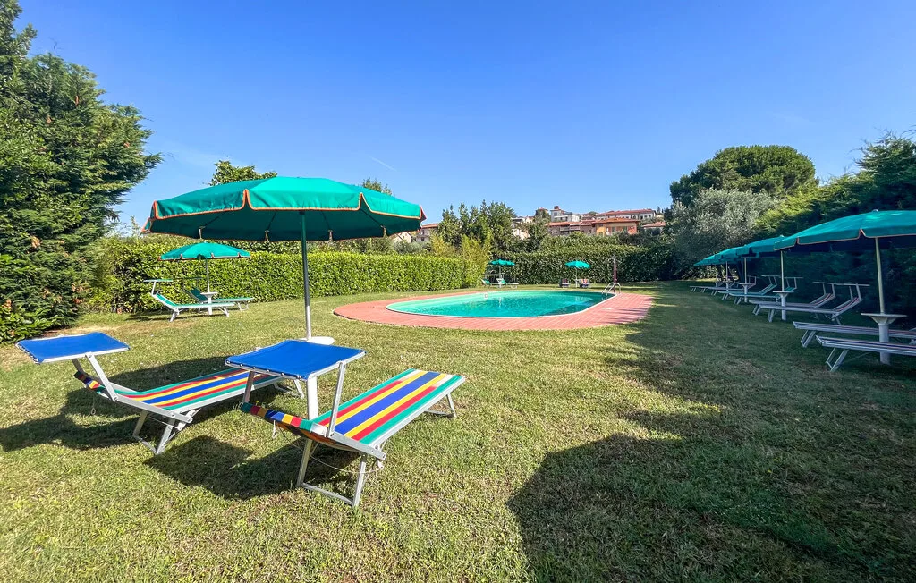 Una piscina al aire libre está rodeada de césped, tumbonas y sombrillas.