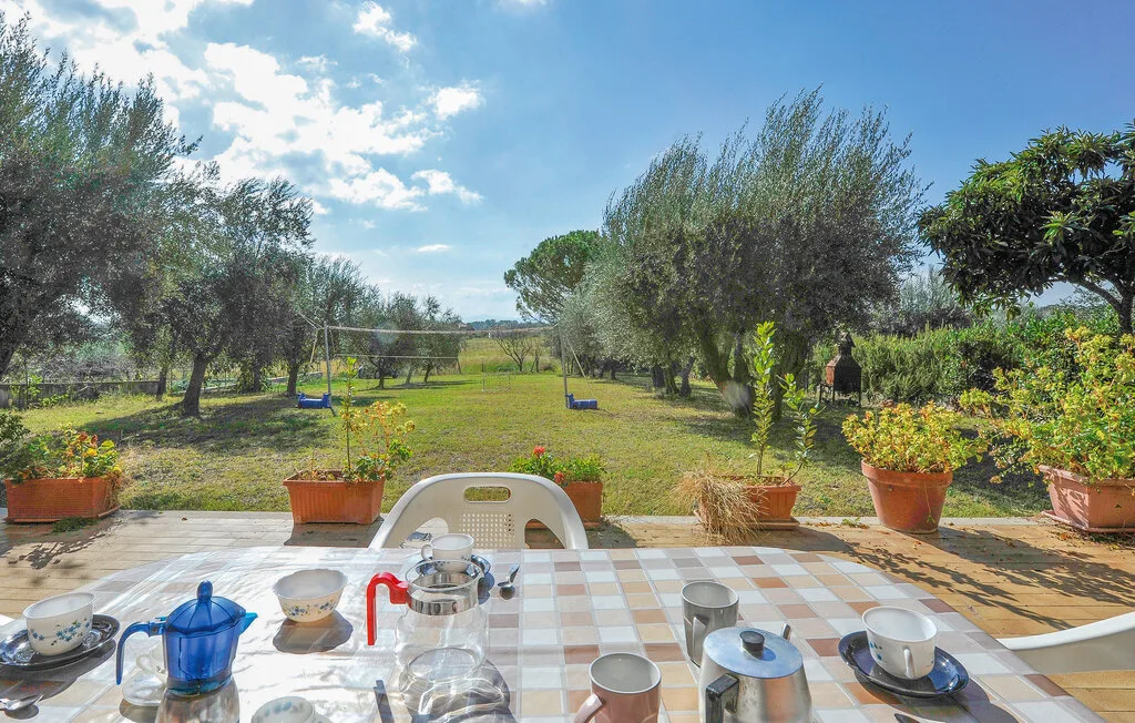 A tiled outdoor table overlooks a grassy garden with trees and shrubs.