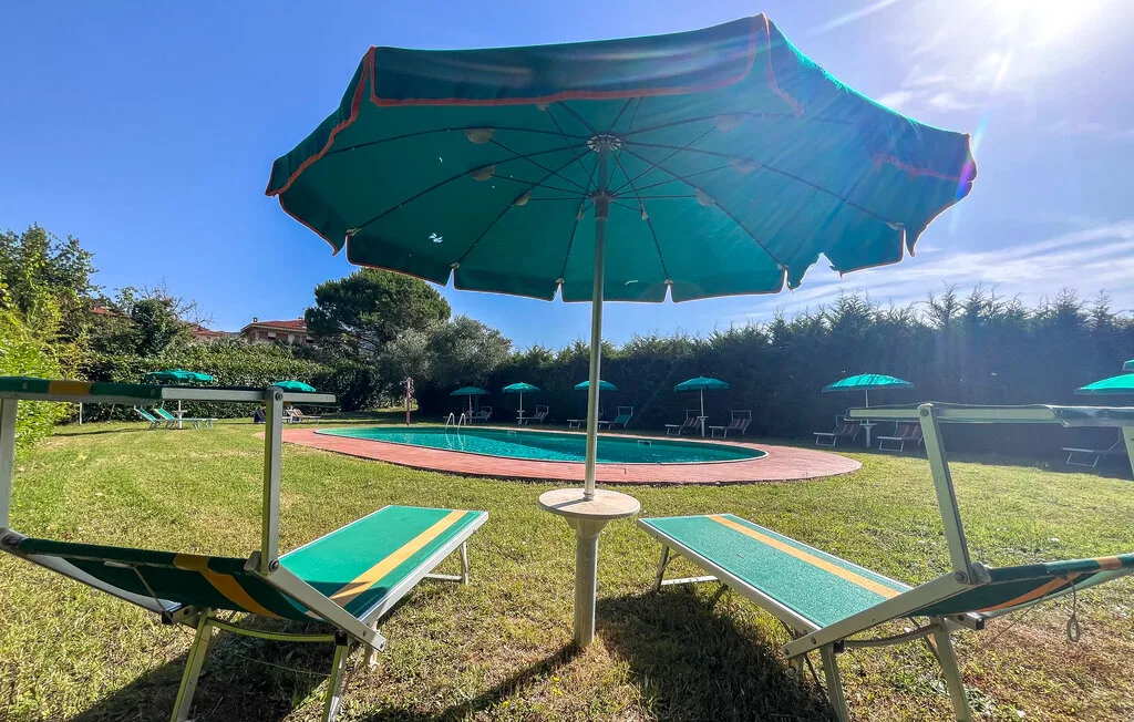 Una piscina al aire libre con tumbonas bajo una sombrilla grande.