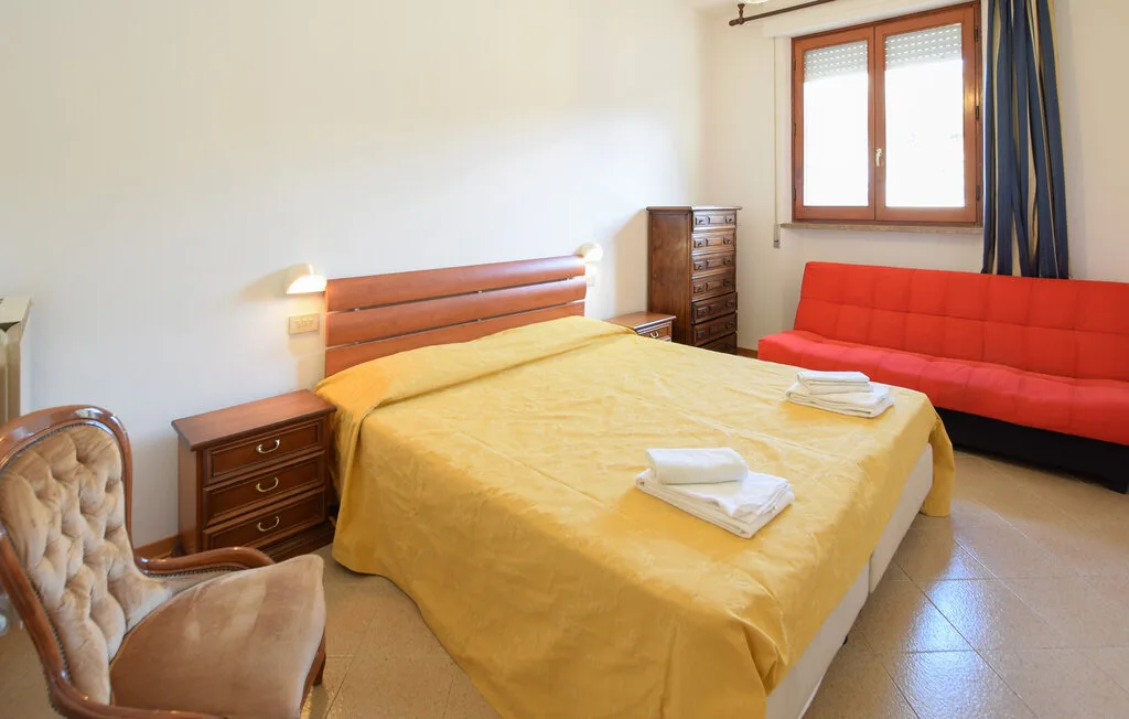 A bedroom with a double bed and red seating beside a window.