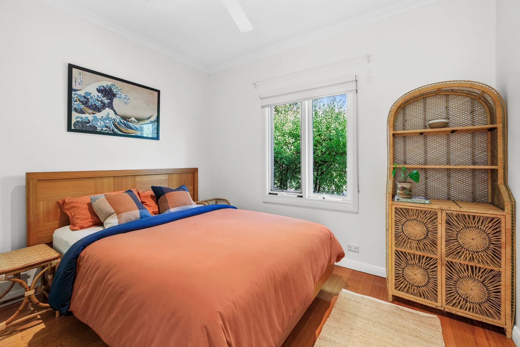 A bedroom with a bed dressed in rust-colored bedding and a wicker cabinet.