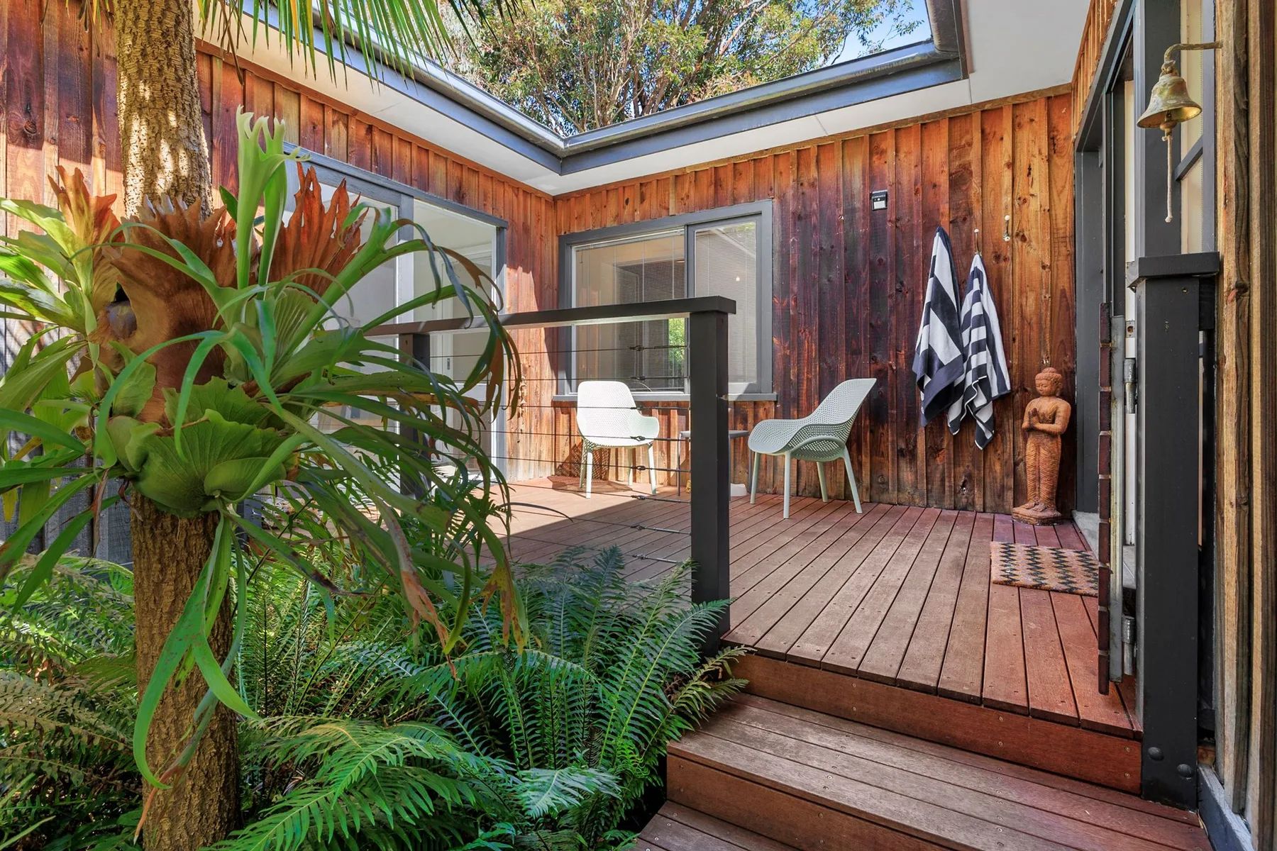 A wooden patio with outdoor seating sits beneath a glass roof.