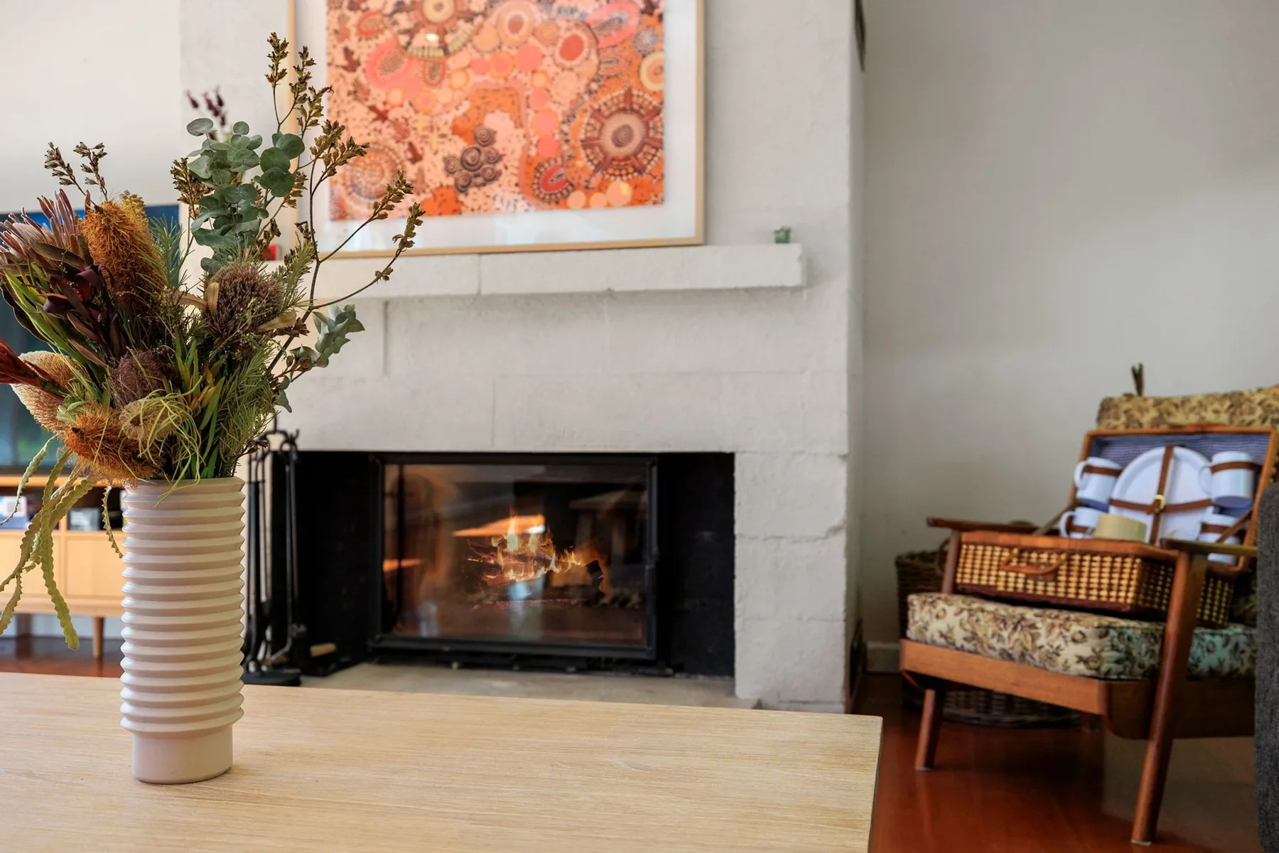 A living room with a lit fireplace and colorful artwork above the mantel.