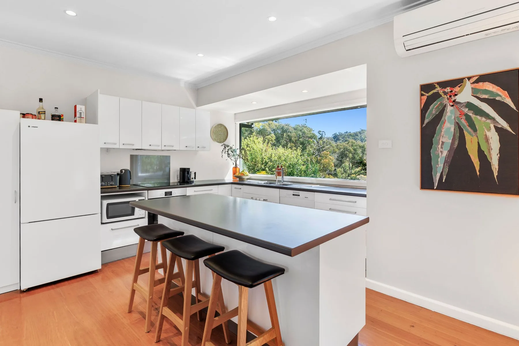 A bright kitchen with a large island and a wide window overlooking greenery.