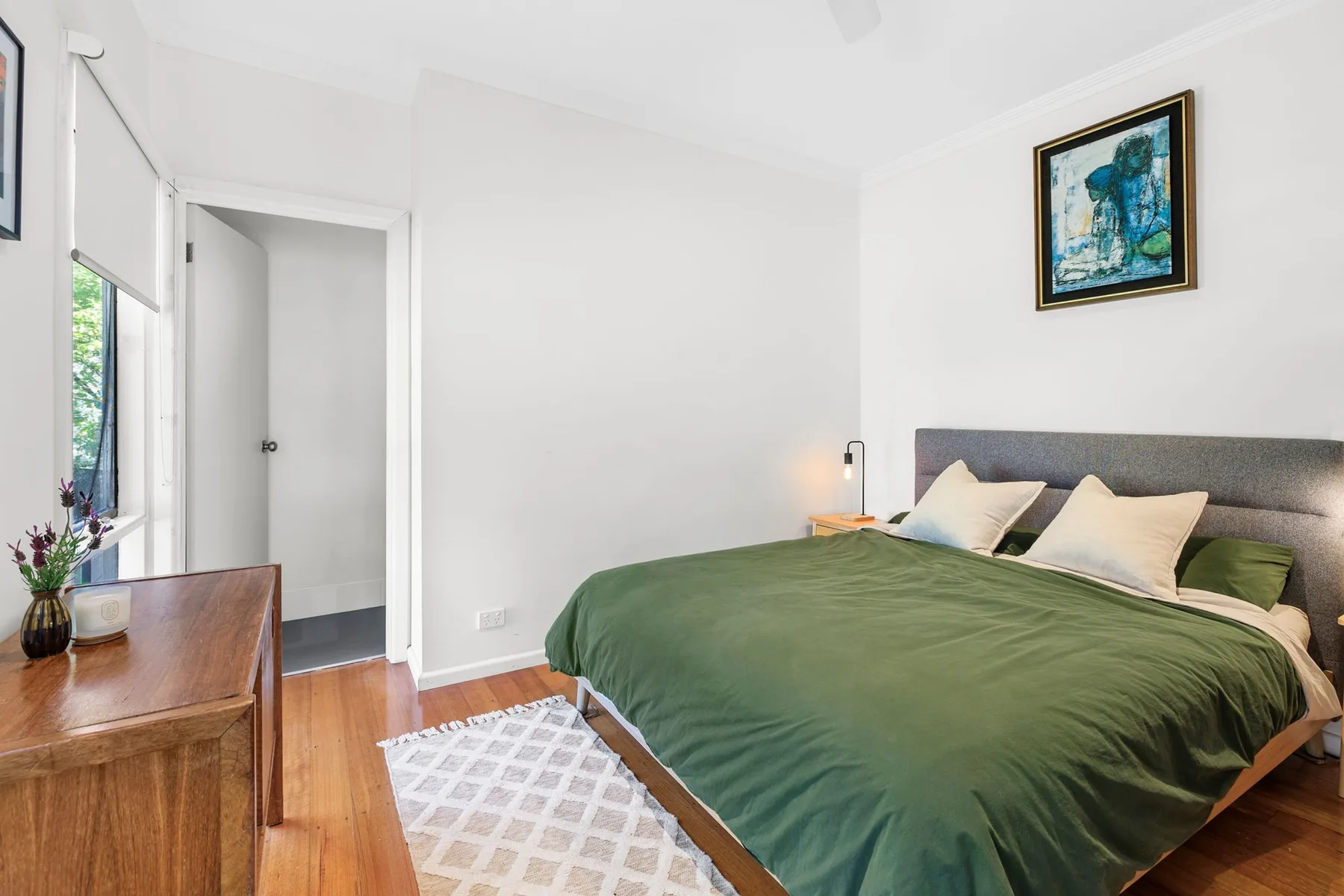 A bedroom with a bed covered in a green blanket and a framed picture above it.