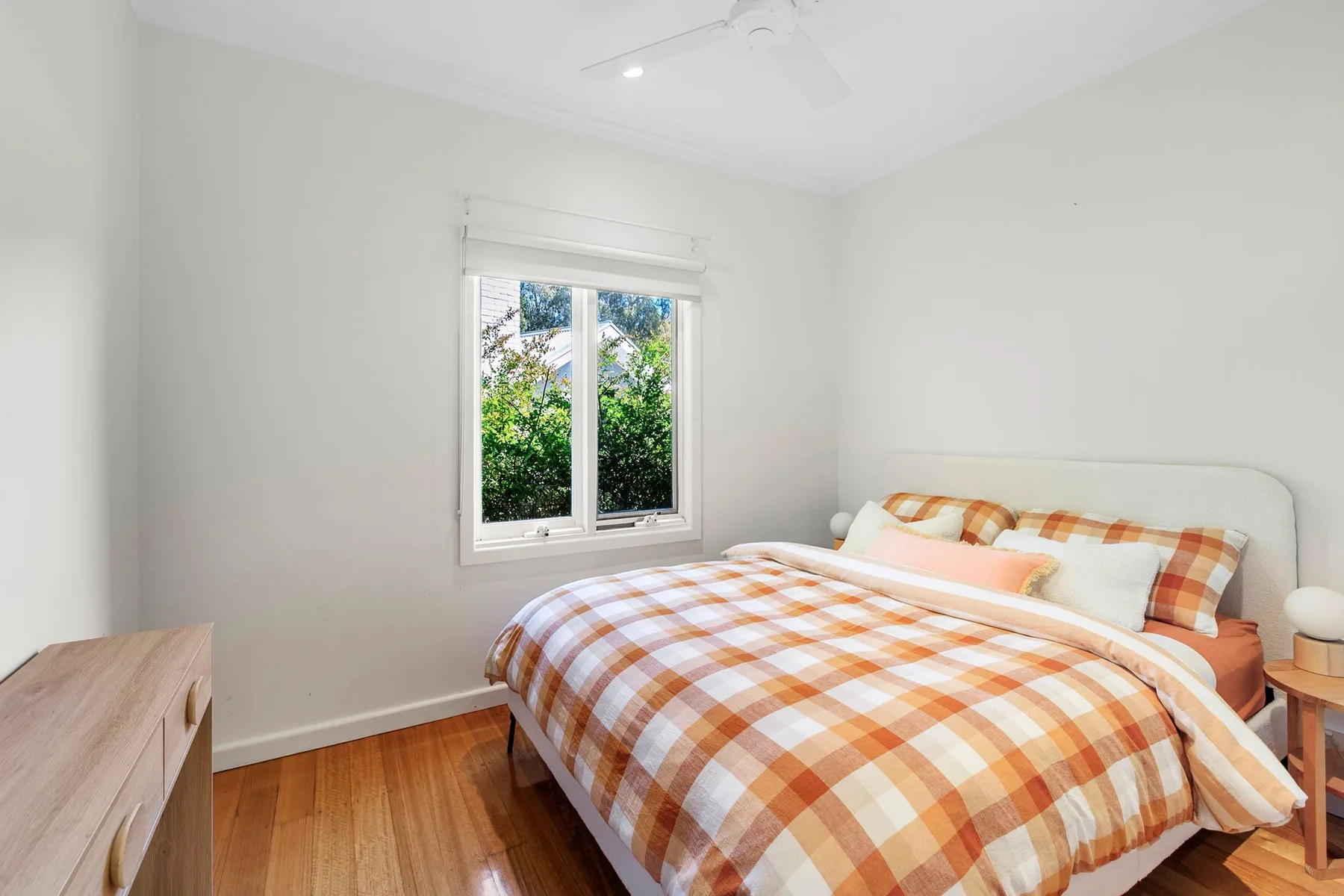 A bright bedroom with a bed dressed in orange-and-white checked bedding beside a window.