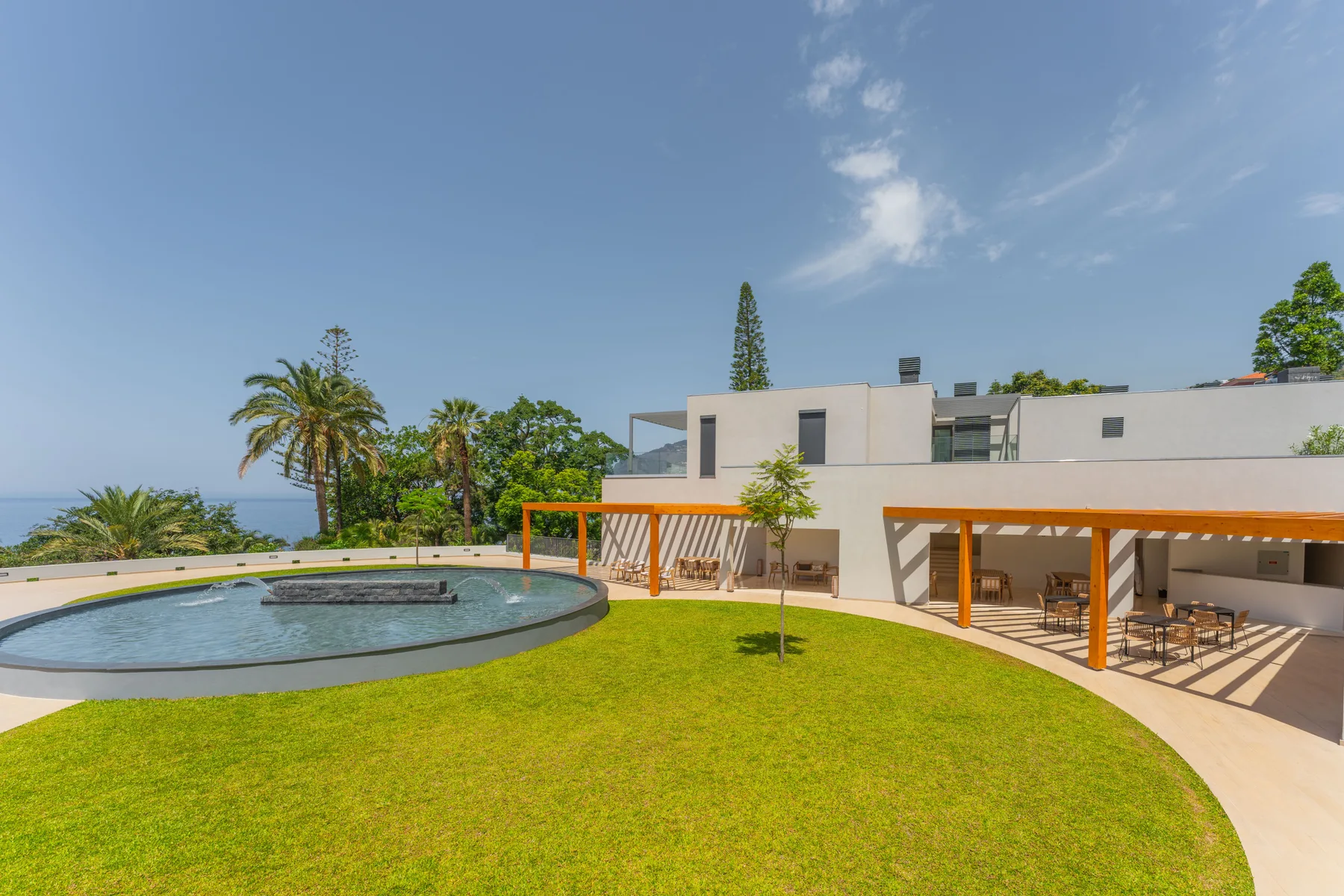 Un patio ajardinado cuenta con una piscina redonda, césped verde y edificios modernos.