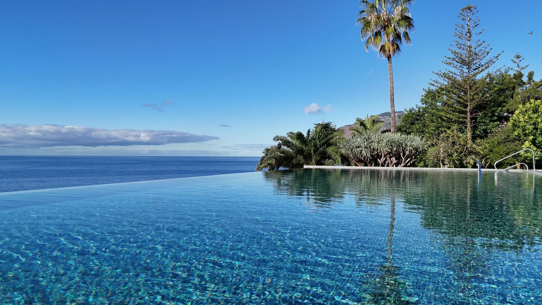 Una piscina infinita mira al océano bajo un cielo azul despejado.