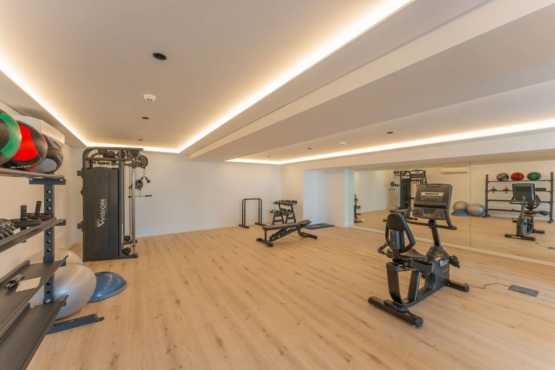Una amplia sala de fitness con máquinas de ejercicio y una pared de espejo.