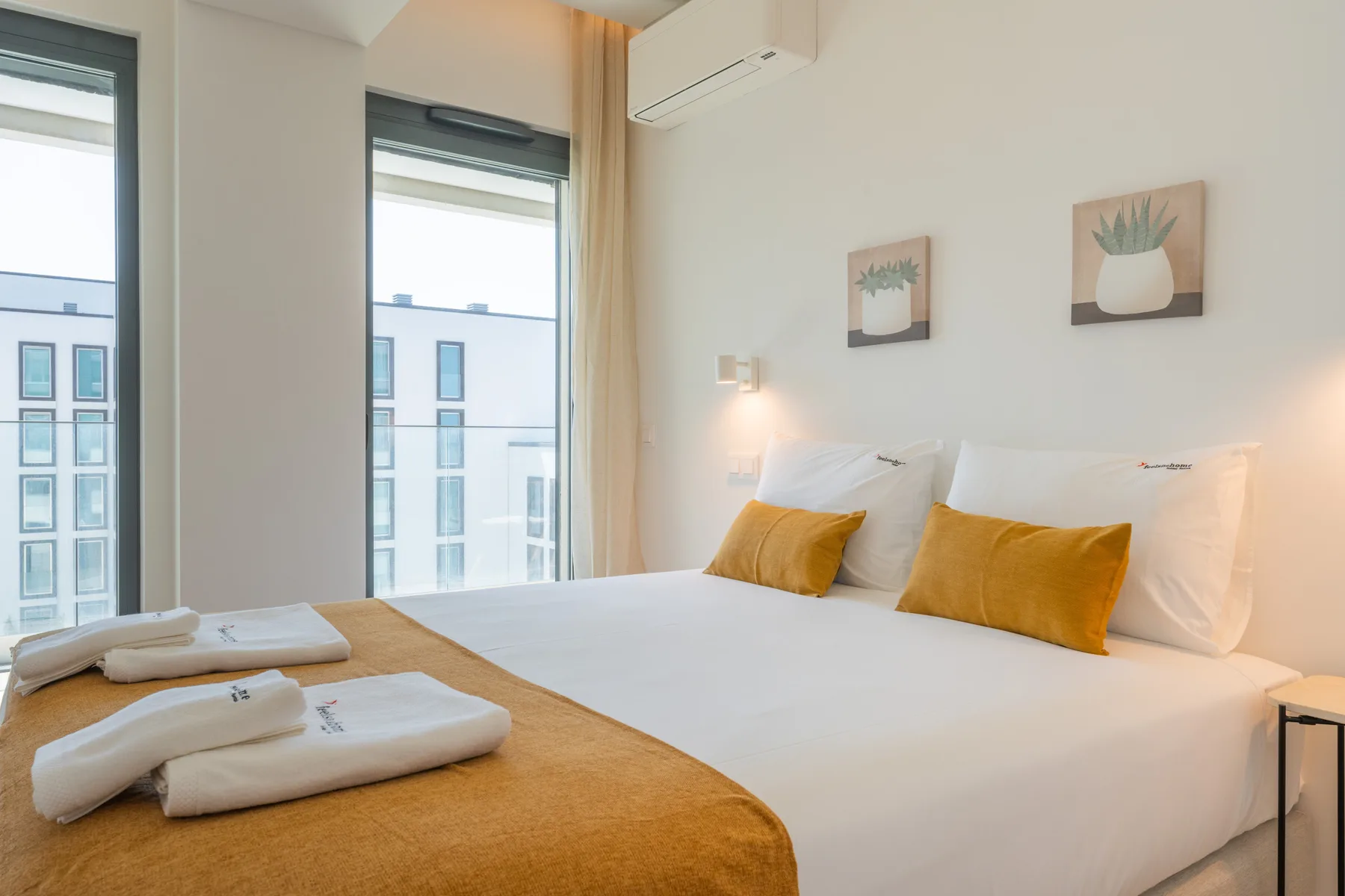 Un dormitorio luminoso con una cama tendida y ventanas altas.