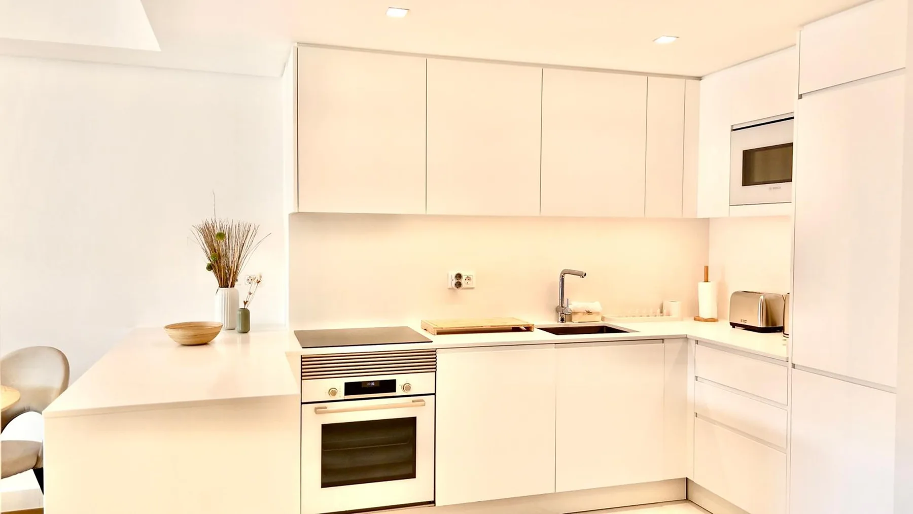 Una cocina moderna y luminosa con armarios blancos y electrodomésticos integrados.