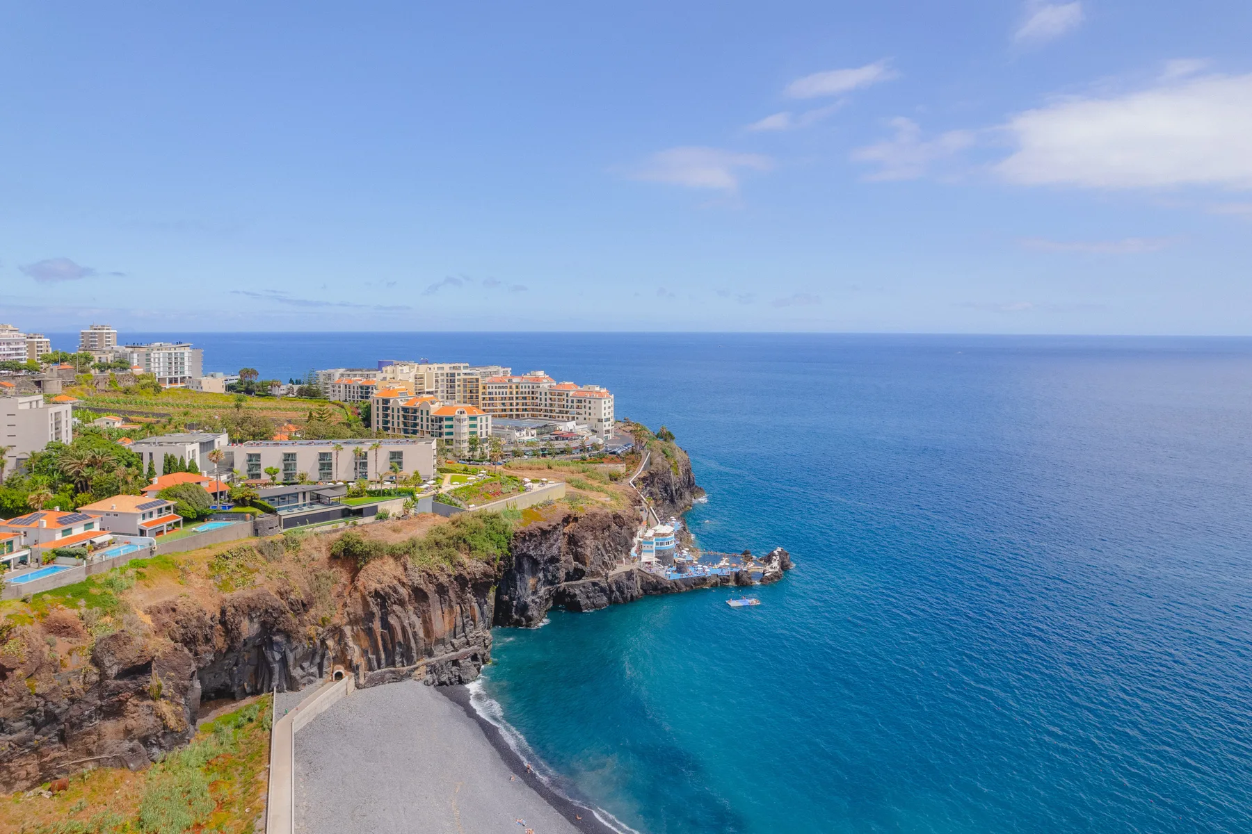 Vista costera de edificios junto a una orilla rocosa sobre el mar azul.