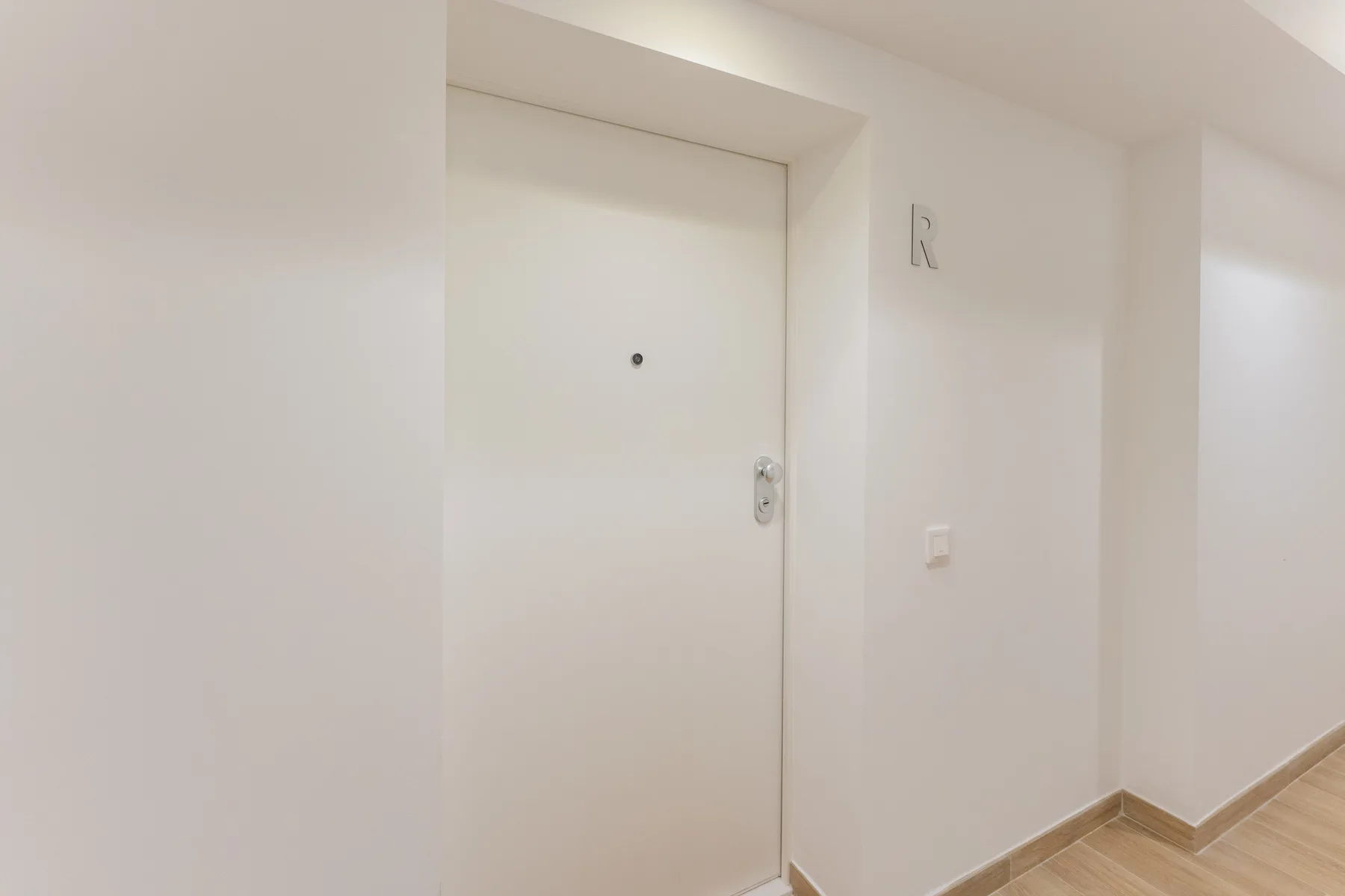 Una puerta blanca da a un pasillo interior luminoso.