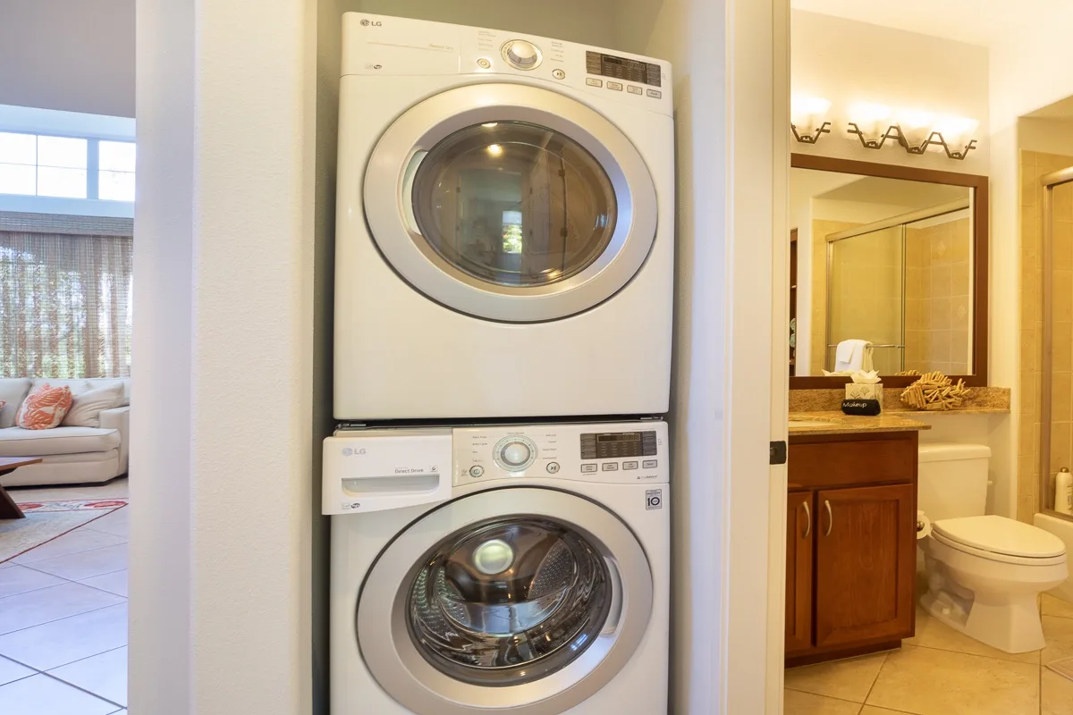 Una zona de lavandería con lavadora y secadora apiladas junto a un baño abierto.