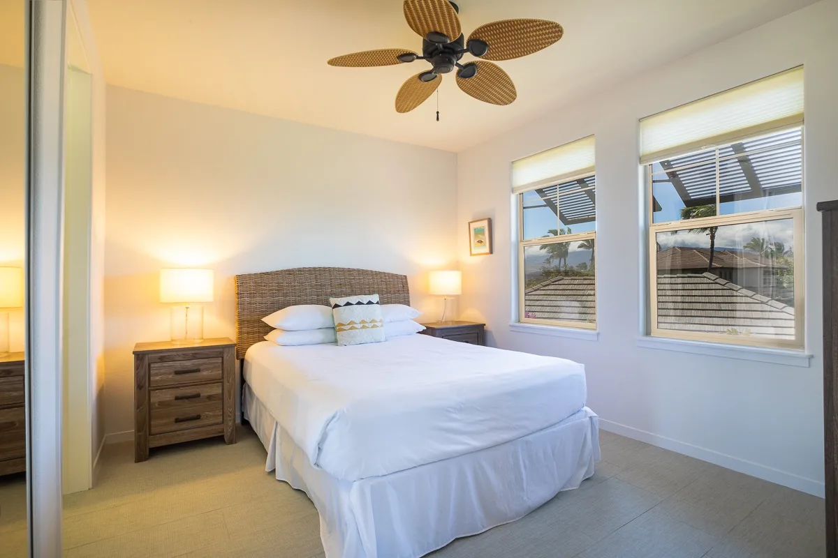 Un dormitorio luminoso con una cama bien tendida y ventanas grandes.