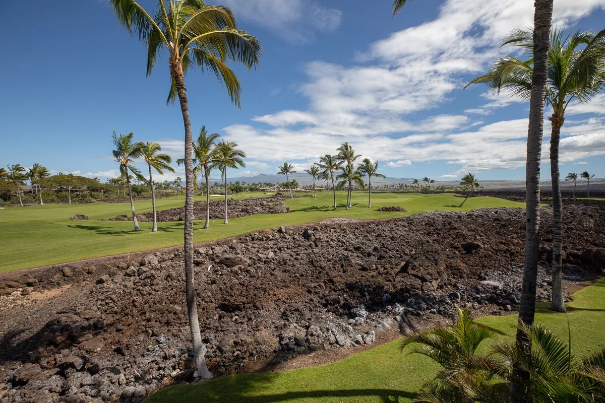 Un campo de golf tropical con palmeras y un paisaje rocoso bajo un cielo azul.