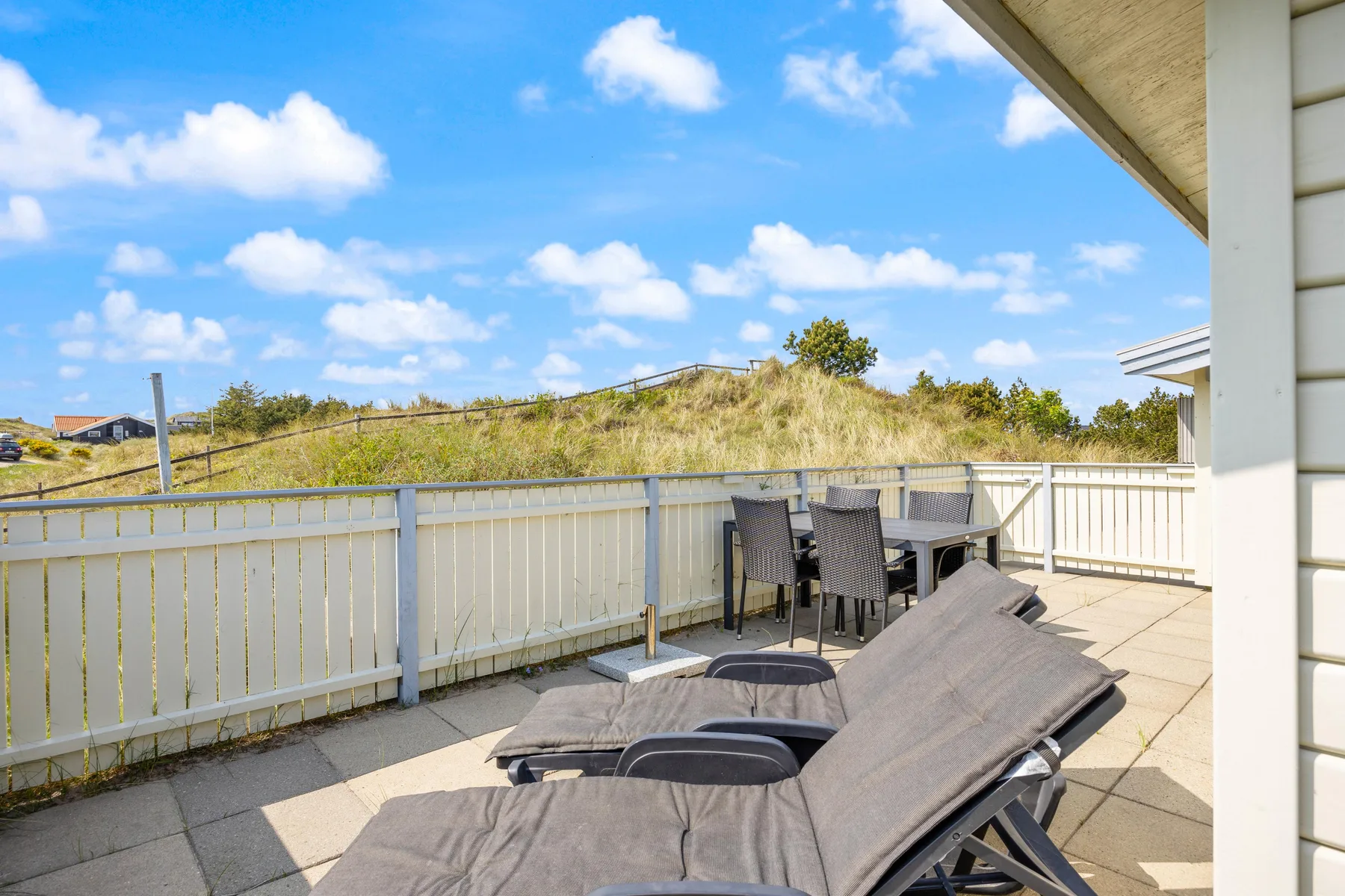 Una terraza soleada con asientos y vistas a dunas cubiertas de hierba.