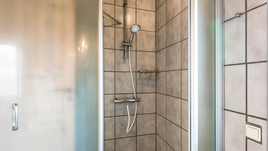 Una ducha con azulejos, ducha de mano y controles montados en la pared.