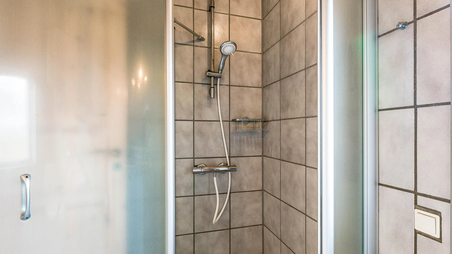 Una zona de ducha con azulejos, ducha de mano y paneles de vidrio.