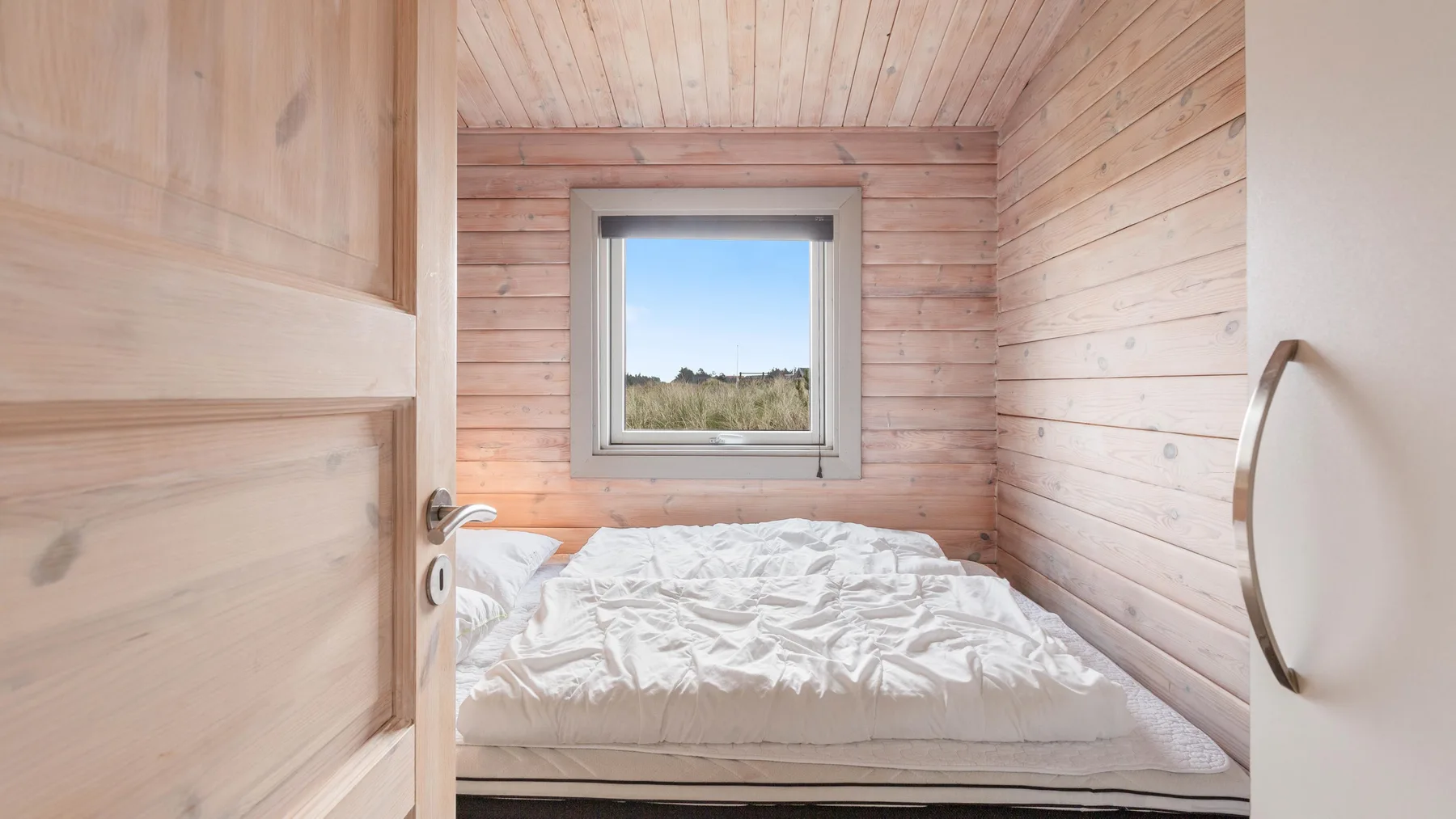 Dormitorio con una cama bajo una ventana en una habitación revestida de madera.