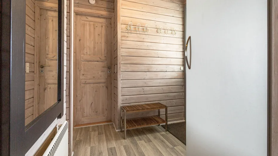 Una entrada revestida de madera con un banco pequeño junto a un espejo de cuerpo entero.