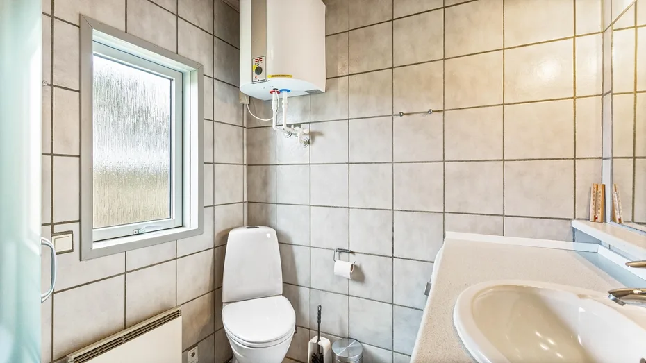 Un baño con azulejos, inodoro, lavabo y ventana esmerilada.