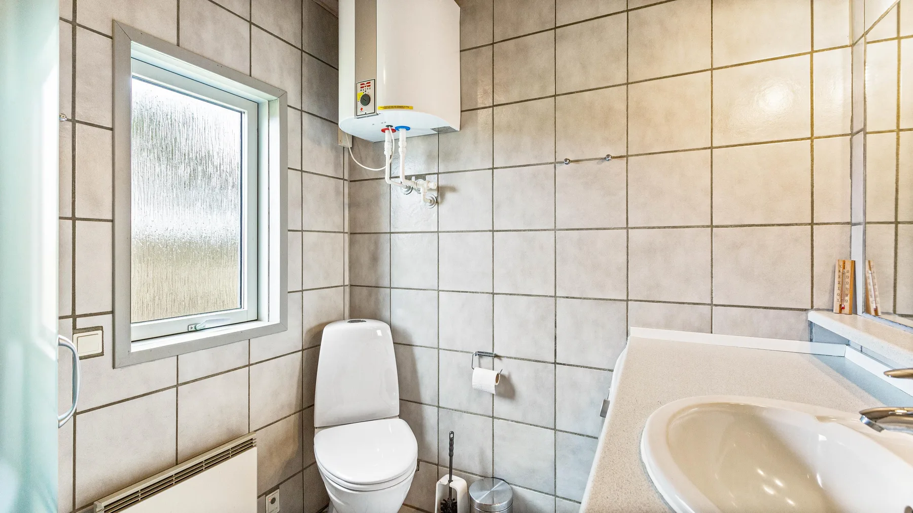 Un baño alicatado con inodoro, lavabo y ventana translúcida.