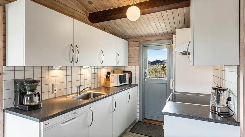 Una cocina luminosa con gabinetes blancos, encimeras oscuras y una puerta con ventana.