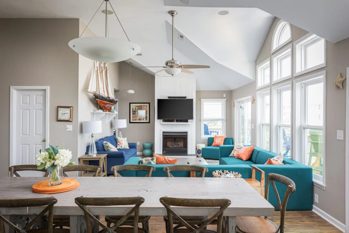 A bright living room with teal seating, a television, and tall windows.